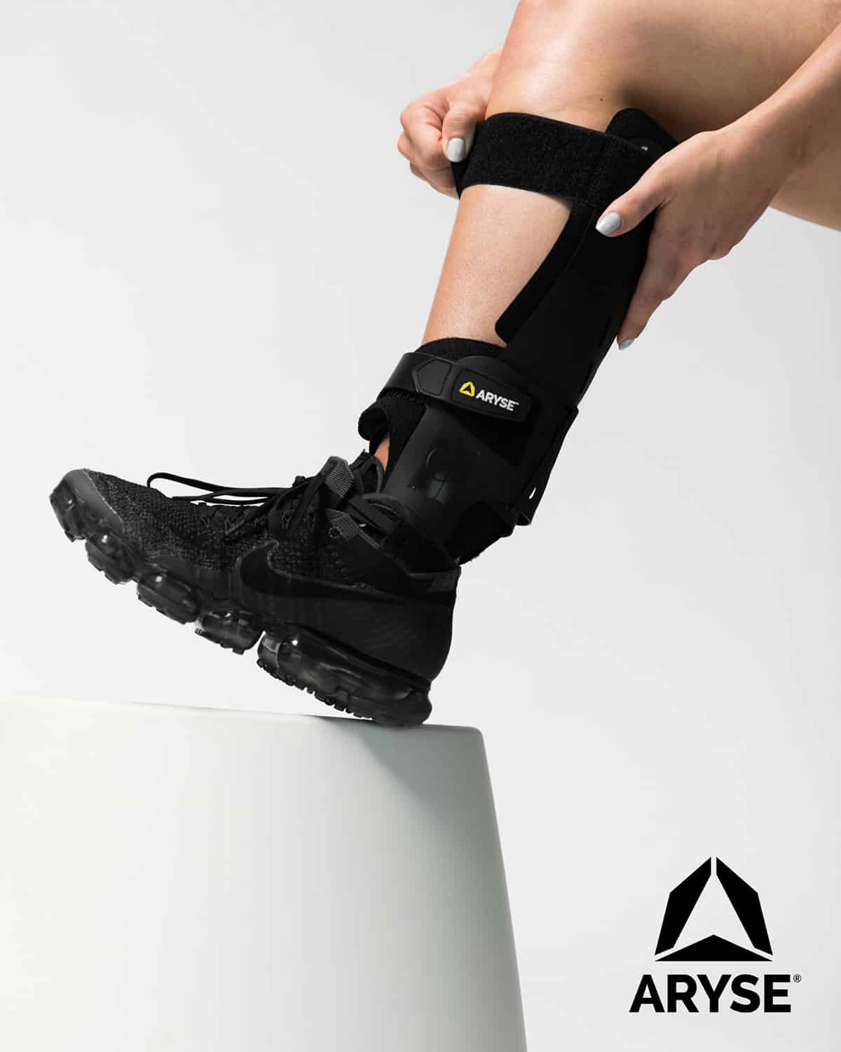 A woman wearing a black ARYSE METFORCE ANKLE on a white pedestal purchased from ARTIK Medical Supply.