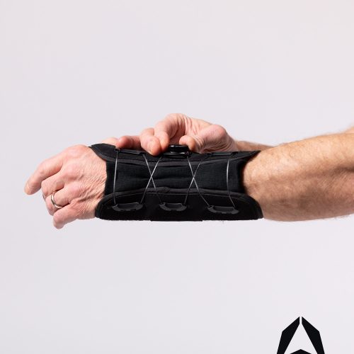 A person holding a black PURESPEED+® WRIST brace on a white background.