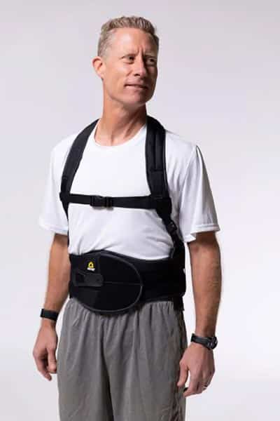 A man wearing a back brace standing in front of a white background.