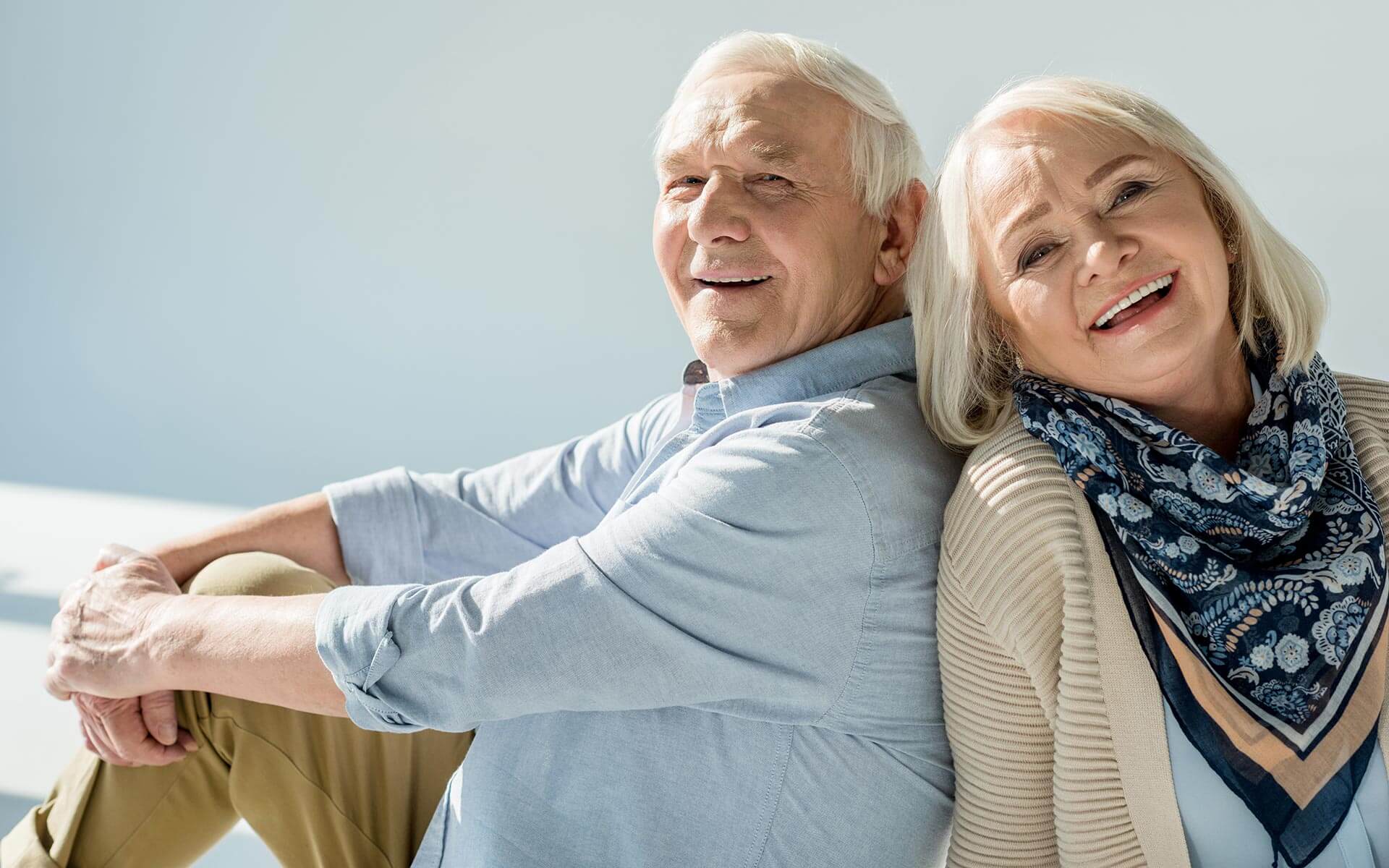 An older couple is sitting on a chair and smiling.