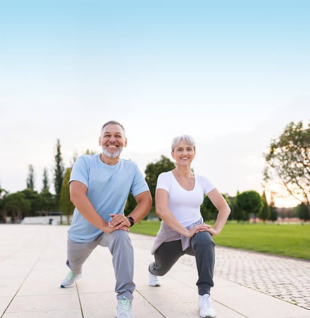 An older couple doing squats in a park.